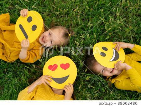 Three funny happy girls hide and look out from behind the faces of emoticons with different emotions Three funny happy girls hide and look out from behind the faces of emoticons with different emotions 89002480