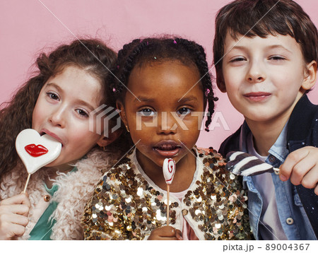 lifestyle people concept: diverse nation children playing together, caucasian boy with african little girl holding candy happy smiling 89004367