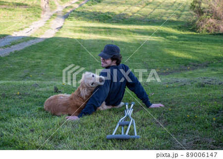Old Golden Retriever dog rests on a hill with a young man with crutches Old Golden Retriever dog rests on a hill with a young man with crutches 89006147