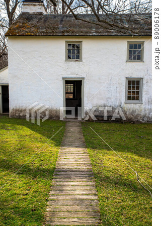 Idyllic path leads through grass to open door of whitewashed stone cottage 89006178