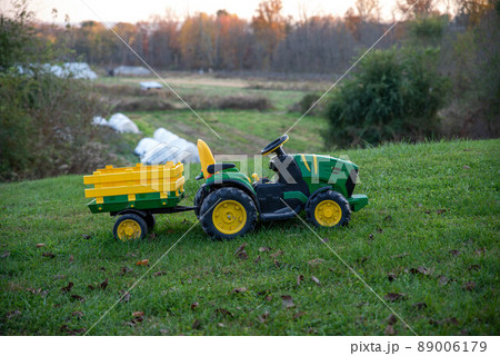 Child's toy riding tractor in green grass yard with farm background Child's toy riding tractor in green grass yard with farm background 89006179