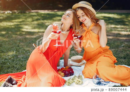 Beautiful girl in a red dress. Women sitting in a summer park. 89007444
