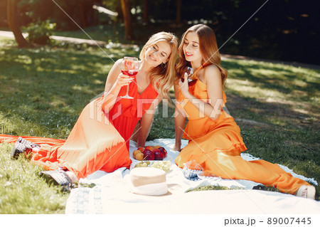 Beautiful girl in a red dress. Women sitting in a summer park. 89007445