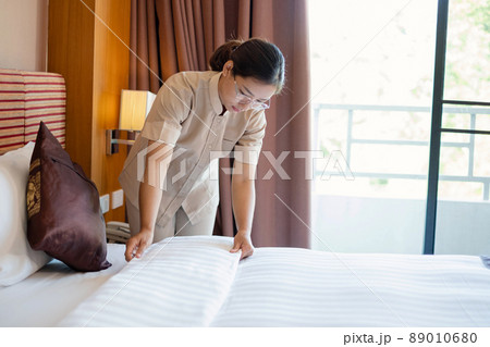 The hotel maid cleans and makes the bed in the hotel room The hotel maid cleans and makes the bed in the hotel room 89010680