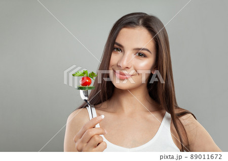 Portrait of attractive young smiling woman eating vegetable salad and holding fork in hand  89011672
