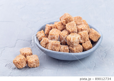 Cubes of brown sugar or cane sugar in bowl and on gray background, horizontal 89012734