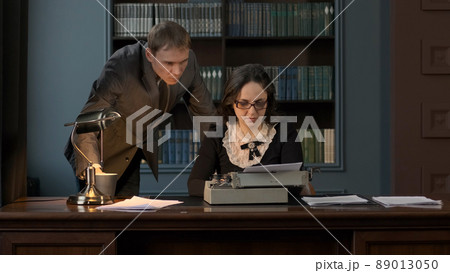 Boss Drinking Coffee or Tea while Dictating Text to Write to Secretary. Female Using Retro Typing Machine in the Office 89013050