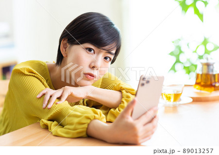 スマホを見る若い女性　部屋でスマホを使う若い女性　ライフスタイル　スマホ　スマートフォン 89013257