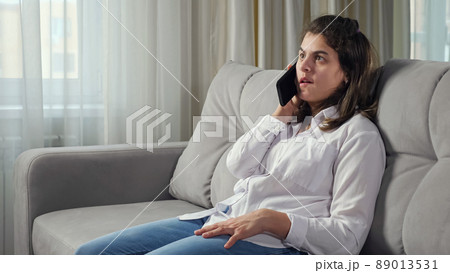 woman talks on mobile phone sitting on sofa at home 89013531