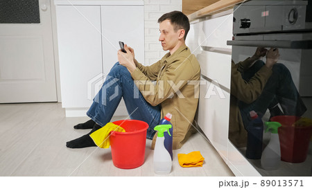 Man takes break after cleaning kitchen using mobile phone Man takes break after cleaning kitchen using mobile phone 89013571