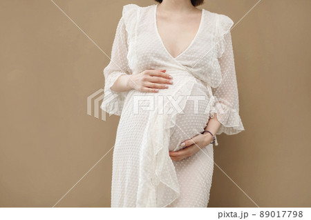 Attractive pregnant woman in white dress on beige background. 89017798