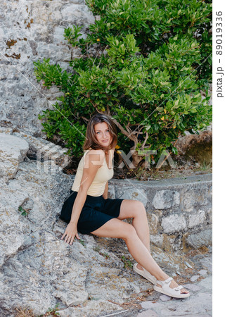 Beautiful girl sits on the stone wall of the old town of Budva . The girl sits on a stone parapet, Budva, Montenegro Beautiful girl sits on the stone wall of the old town of Budva . The girl sits on a stone parapet, Budva, Montenegro 89019336