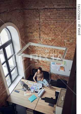 High angle view of relaxed woman designer taking a break while working on interior design project, sitting at the table in modern office 89022591