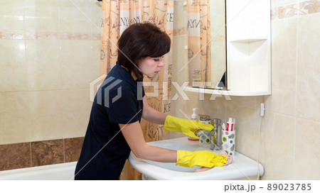 An adult brunette woman is cleaning the bathroom, washing the sink 89023785