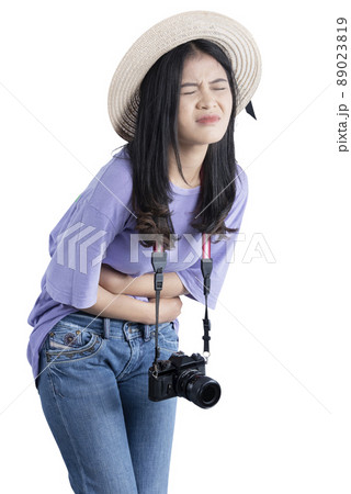 Asian woman with hat and camera having stomach pain while traveling 89023819