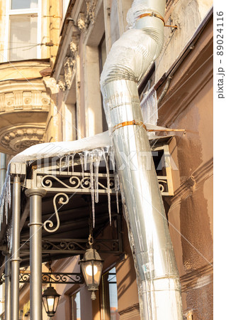 Sharp icicles a lot and melted snow hanging from eaves of roof and downpipe. Vertical photo. 89024116
