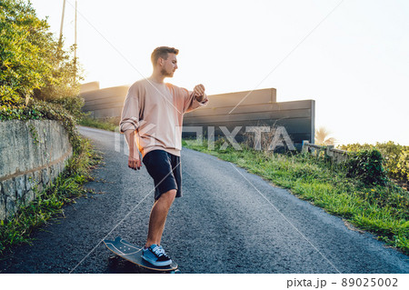 Professional man sportsman with skateboard enjoying evening training on asphalt road 89025002