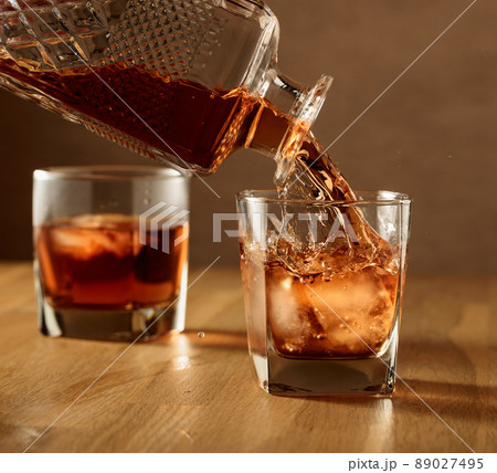Whiskey is poured into a dammed glass with ice. Whiskey is poured into a dammed glass with ice. 89027495