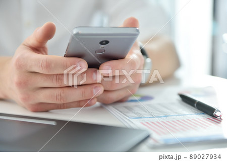 Manager sitting in office and writes message on smartphone. 89027934