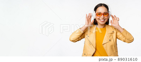 Beautiful asian girl, laughing happy, listening music in headphones, standing over white background 89031610