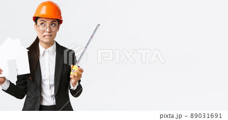 Indecisive asian female architect, construction engineer in helmet and business suit holding house maket and tape measure, biting lip unsure, looking away thoughtful, searching solution Indecisive asian female architect, construction engineer in helmet and business suit holding house maket and tape measure, biting lip unsure, looking away thoughtful, searching solution 89031691
