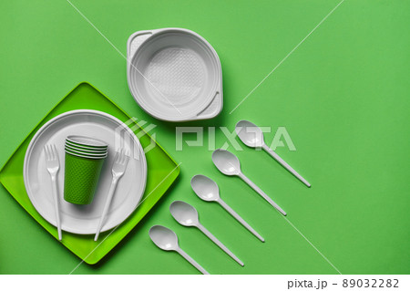 Colorful plastic disposable tableware on green background with copy space. The concept of picnic utensil. Top view. Selective focus. Close-up. 89032282