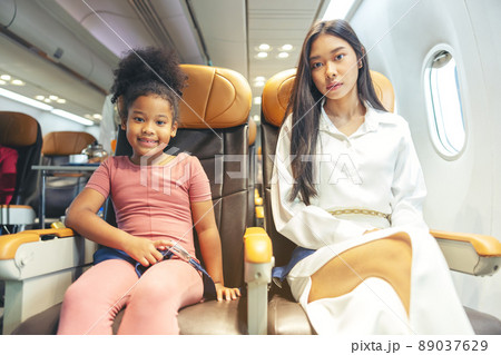 A happy little child and woman are seated in a passenger airliner. A happy little child and woman are seated in a passenger airliner. 89037629
