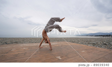 Shirtless caucasian man doing backflip on pebble beach. Shirtless caucasian man doing backflip on pebble beach. 89039340