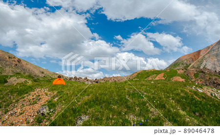 Camping on a summer green high-altitude plateau. Orange tent in a green mountain hollow. Camping on a summer green high-altitude plateau. Orange tent in a green mountain hollow. 89046478