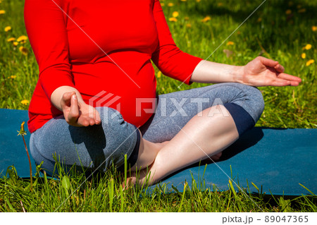 Pregnant woman doing asana Sukhasana outdoors 89047365