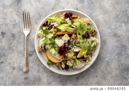 Salad with blue cheese, apples, arugula and nuts with spicy dressing on a grey background. Healthy eating. Salad with blue cheese, apples, arugula and nuts with spicy dressing on a grey background. Healthy eating. 89048285