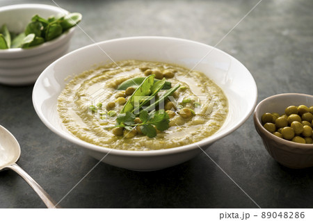Green cream soup with green fresh peas in white plate on dark background. Healthy, vegan food Green cream soup with green fresh peas in white plate on dark background. Healthy, vegan food 89048286
