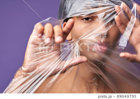 Close up horizontal portrait of young man tear up plastic bag with look eyes. Freedom of transgender 89049795