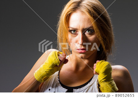 Muscular young athletic sportswoman in sportswear with bands or gloves in the gym on a dark background. Sports martial arts. Copy space for ads for fitness nutrition, sports equipment or exercise.  89052655