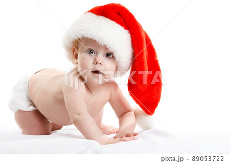 Adorable child is sitting on floor, wearing red Christmas cap, isolated over white Adorable child is sitting on floor, wearing red Christmas cap, isolated over white 89053722