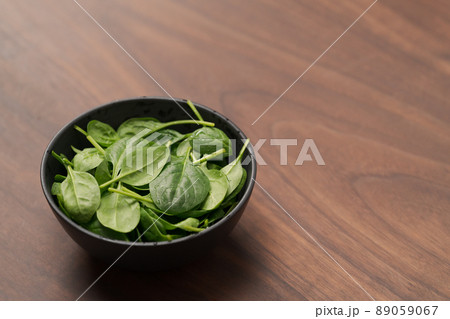 Fresh spinach leaves in black bowl on walnut wood table 89059067