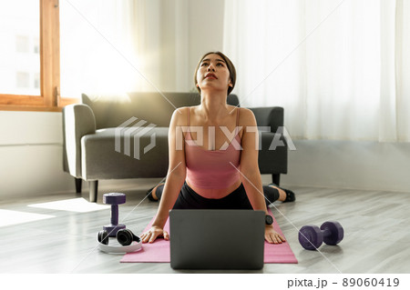 Fitness instructor having virtual yoga class using video call on laptop. Remote yoga teacher leads a lesson for people 89060419