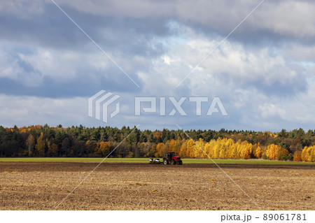 tillage with a red tractor with plows on an agricultural field 89061781