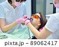 Dentist and assistant applies whitening gel to patient's teeth. 89062417