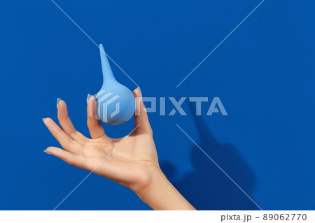 Wellgroomed womans hand holding enema on blue background 89062770