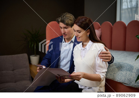 Middle-aged couple in love looking at a catalog of upholstered furniture while visiting a furniture store to buy a sofa, an orthopedic mattress and a new stylish bed. Home interior design concept Middle-aged couple in love looking at a catalog of upholstered furniture while visiting a furniture store to buy a sofa, an orthopedic mattress and a new stylish bed. Home interior design concept 89062909