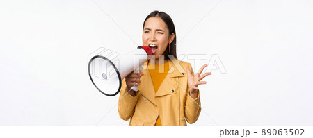 Portrait of young asian woman protester, screaming in megaphone and protesting, standing confident against white background Portrait of young asian woman protester, screaming in megaphone and protesting, standing confident against white background 89063502
