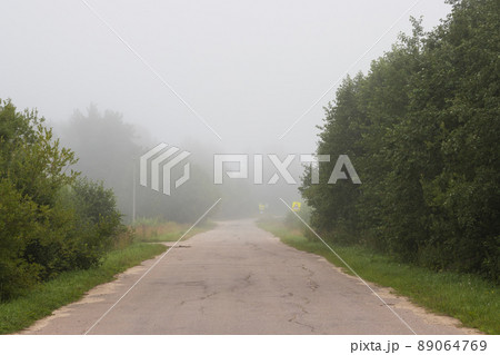 A deserted country road leading into the distance into the fog A deserted country road leading into the distance into the fog 89064769