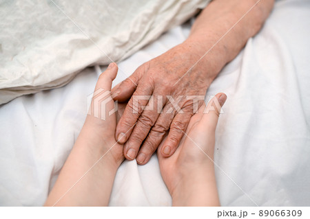 The grandson's hands hold the wrinkled hand of a sick elderly grandmother in a medical clinic. The concept of love and care. Slow movement The grandson's hands hold the wrinkled hand of a sick elderly grandmother in a medical clinic. The concept of love and care. Slow movement 89066309