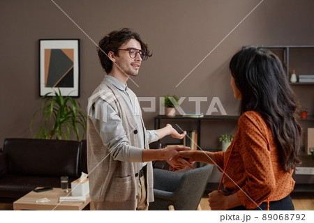 Horizontal medium shot of young psychologist greeting woman shaking hands and offering her to take seat 89068792