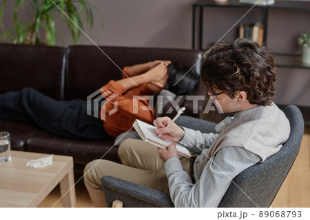 Horizontal high angle shot of professional psychologist listening to his client and writing down notes in notebook 89068793