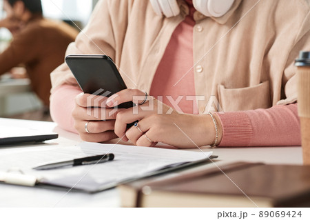 Close-up of unrecognizable woman in rings sitting at desk and checking message on phone 89069424