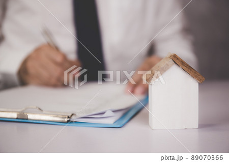 Hands of business man sign agreement buying home while model home on desk. 89070366