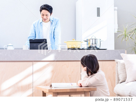 リビングで勉強する子供とキッチンで動画を見るパパ リビングで勉強する子供とキッチンで動画を見るパパ 89071537