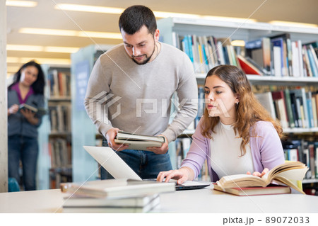 Male librarian helping focused adult student preparing to exam Male librarian helping focused adult student preparing to exam 89072033